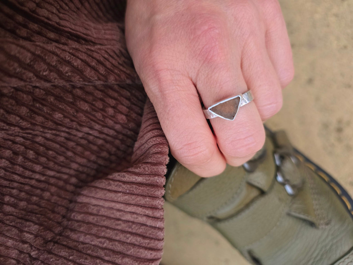 Close-up of the autumnal triangular sea glass ring and textured band worn on a hand