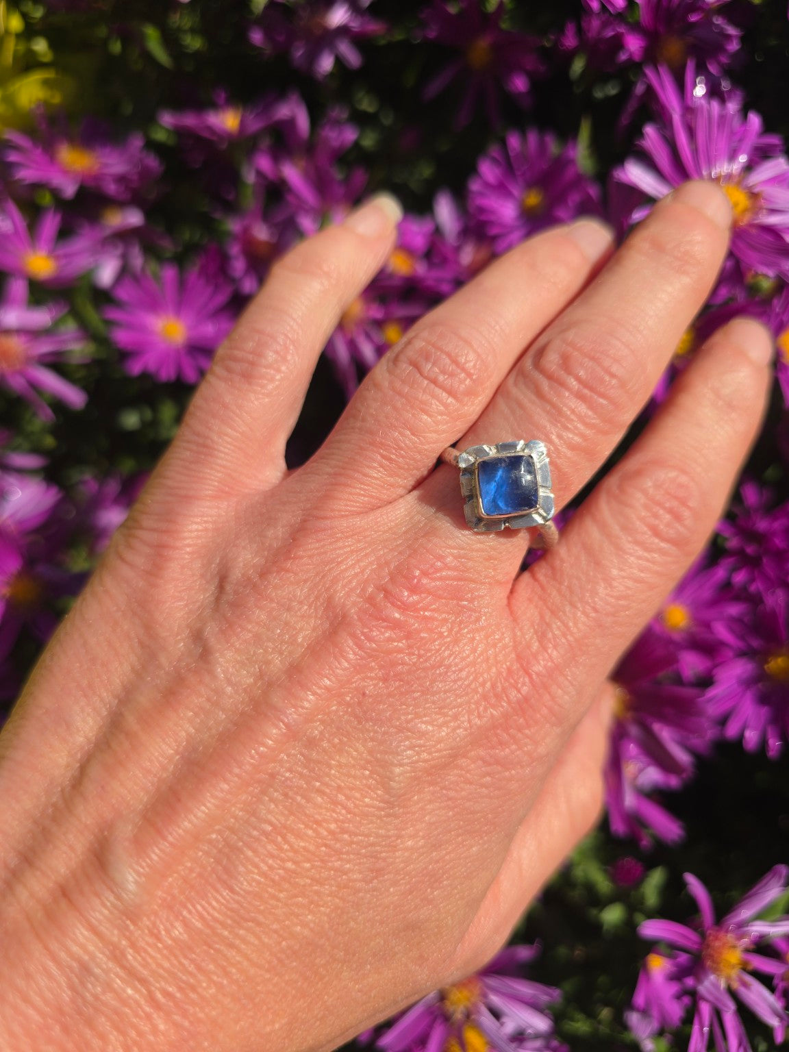 Cobalt blue seaglass adjustable sterling silver ring worn on a hand against purple flowers