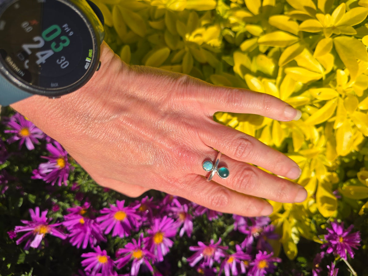 Rockpool adjustable ring with teal seaglass and lab-grown opal worn on a hand against flowers