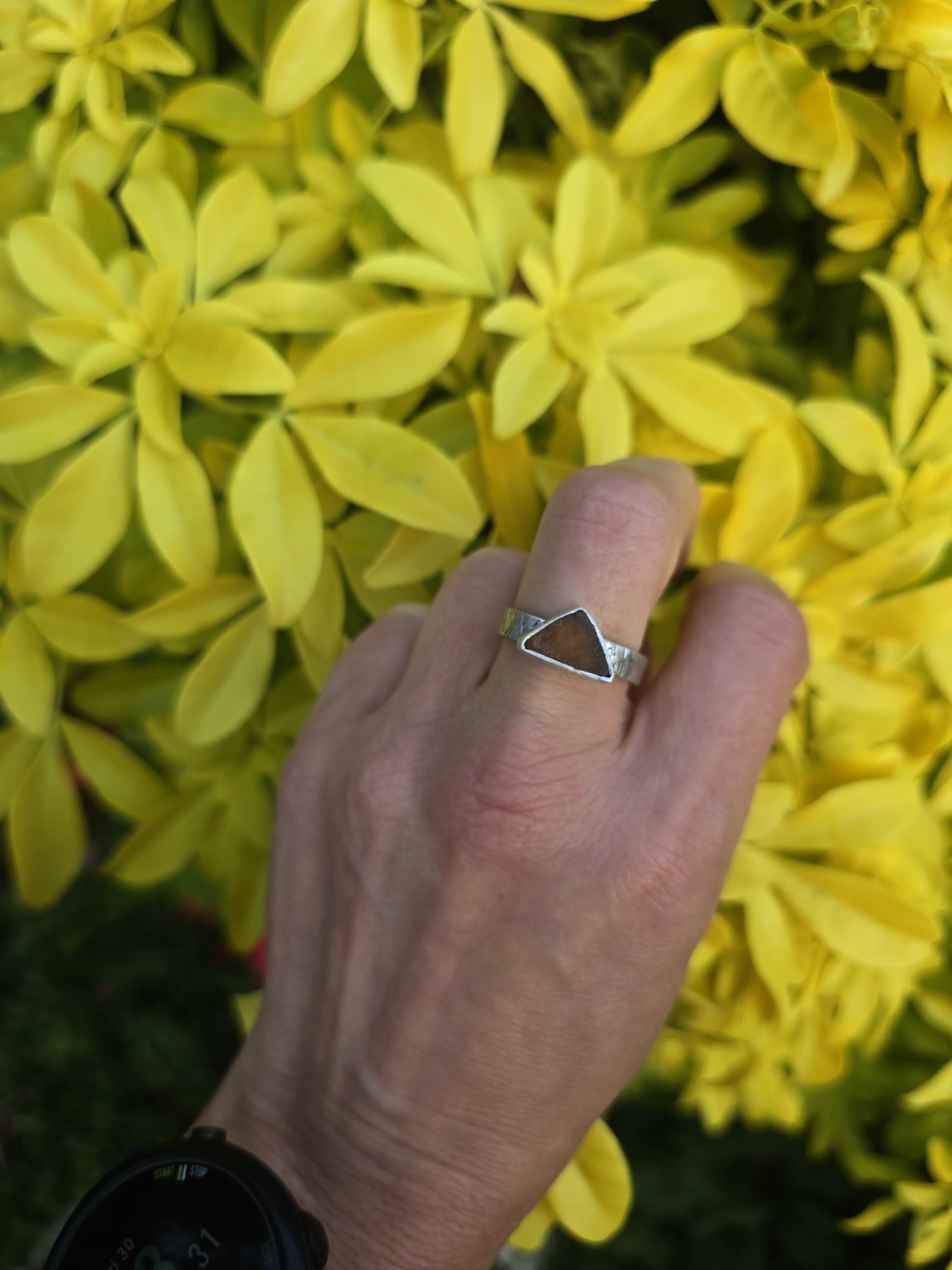 Autumnal dark triangular sea glass ring on a chunky textured band, worn against yellow foliage