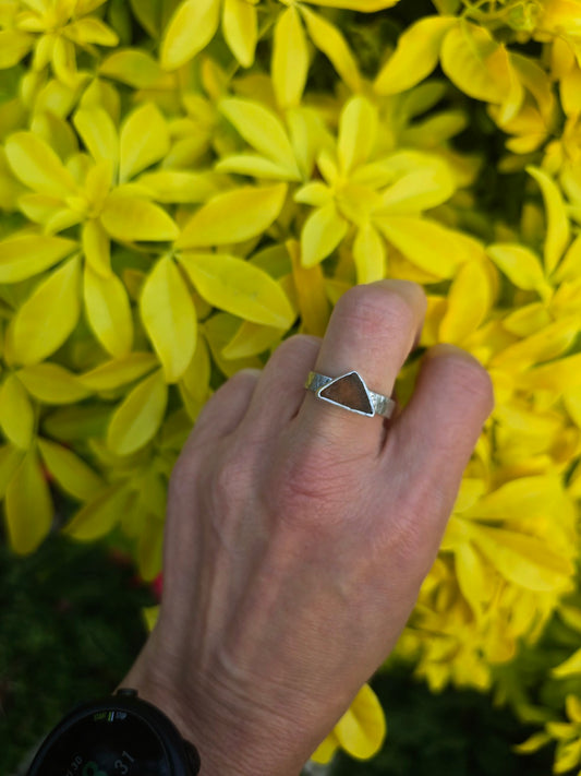 Autumnal dark triangular sea glass ring on a chunky textured band, worn against yellow foliage
