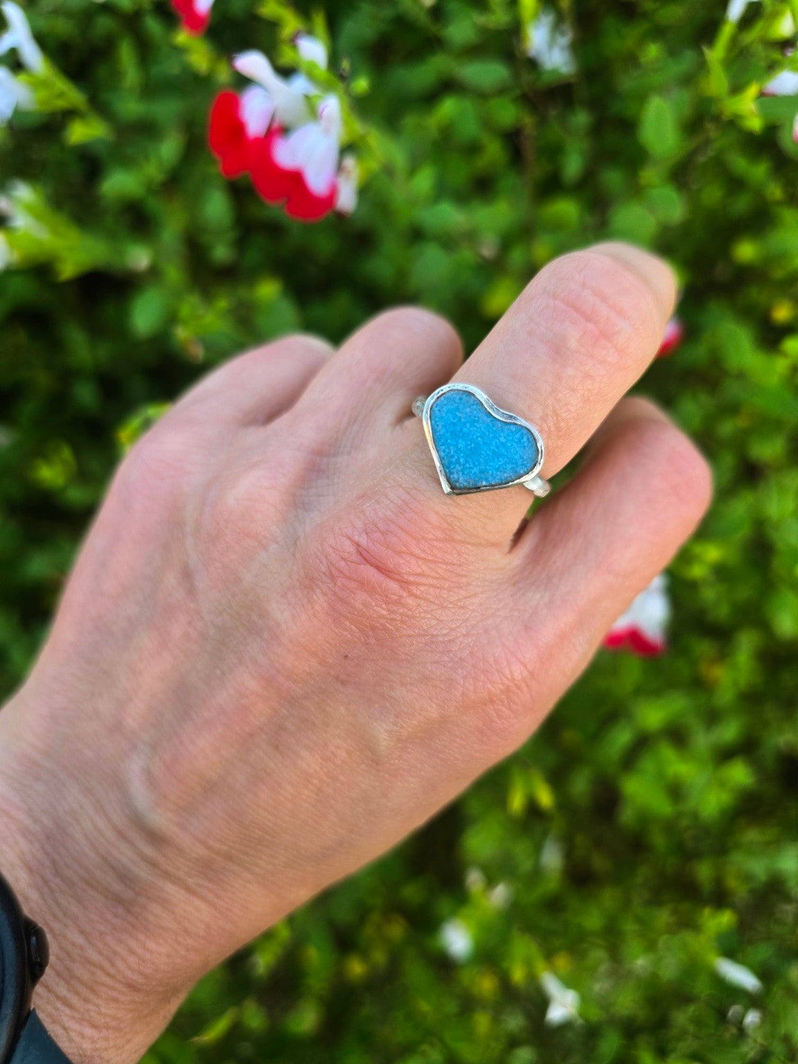 Bright-blue heart-shaped bubble sea glass ring in recycled sterling silver, worn on a hand