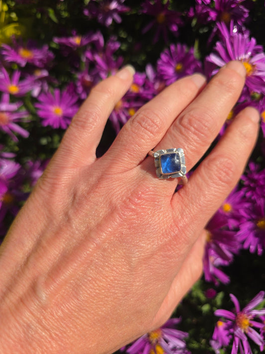 Cobalt blue seaglass adjustable sterling silver ring worn on a hand against purple flowers