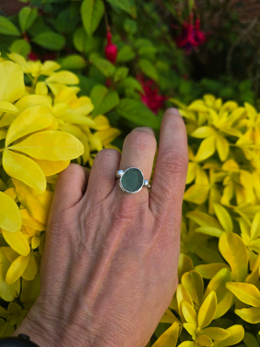 Ocean-blue sea glass ring with silver bobbles on either side, worn on a hand against yellow foliage