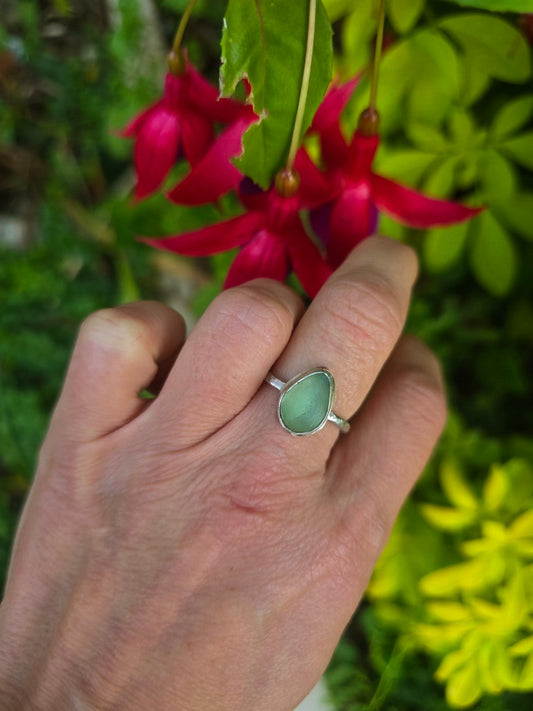Sea green seaglass dainty raindrop ring in recycled sterling silver, worn on a hand beside pink flowers