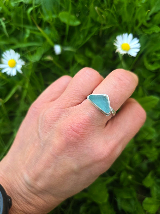 Seafoam coloured seaglass ring in recycled sterling silver, worn on a hand beside daisies